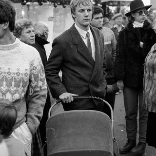 Young man pushing baby stroller in crowded outdoor setting.