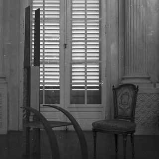 Elegant room with closed louvered windows, ornate chair, and curved desk.