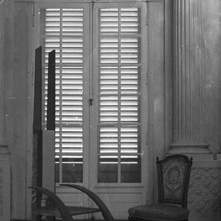 Elegant room with closed louvered windows, ornate chair, and curved desk.