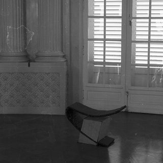 Empty room with classical columns, open shutters, and a lone bench.