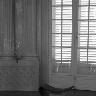 Empty room with classical columns, open shutters, and a lone bench.