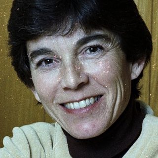 Woman smiling indoors wearing light-colored sweater.