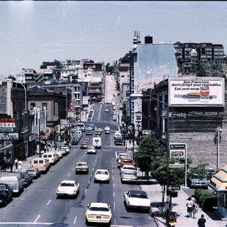 Urban street scene with mid-century traffic and buildings.