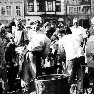 People gathering around a large communal food pot outdoors.