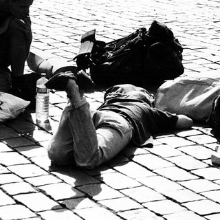 People resting on cobblestone ground with backpacks.