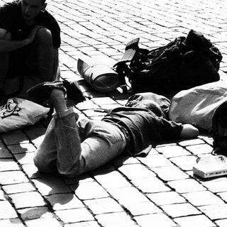 Two people resting on backpacks in public square.