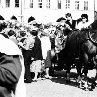 Horse-drawn carriage in crowded street scene.
