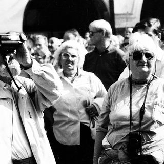 Group of elderly people at outdoor event, holding cameras.