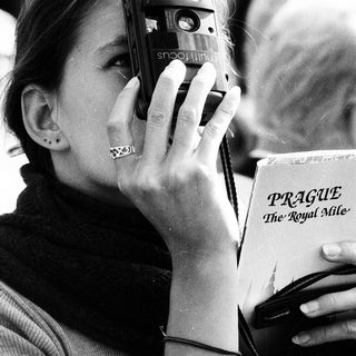 Woman taking photo with vintage camera near Prague guidebook.