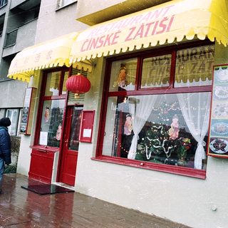 Chinese restaurant with yellow awning, red door, people walking by in rainy weather.
