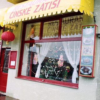 Chinese restaurant with yellow awning, red door, people walking by in rainy weather.