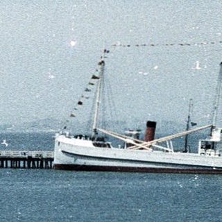 Coastal pier, calm waters, vintage ship, distant city.