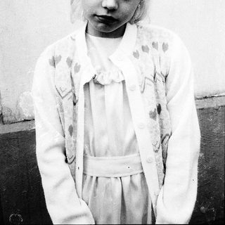 Young girl in vintage dress, serious expression.