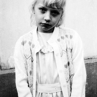 Young girl in vintage dress, serious expression.