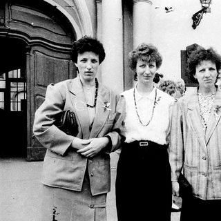 Four women posing together outdoors in formal attire.