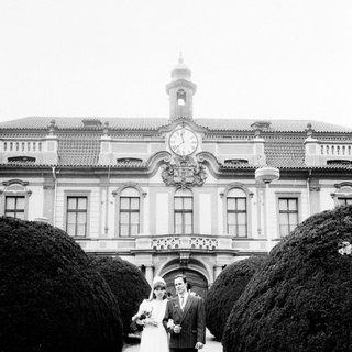 Couple posing in wedding attire outside grand building.