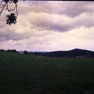 Rural landscape with rolling hills, open field, and cloudy sky.