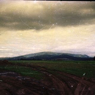 Rural landscape with rolling hills under cloudy sky.