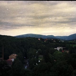 Rural landscape with forested hills, buildings, and industrial chimneys.