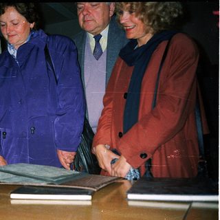 Four individuals signing a large book together.