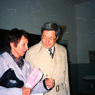 Two people in formal attire examining a handkerchief indoors.