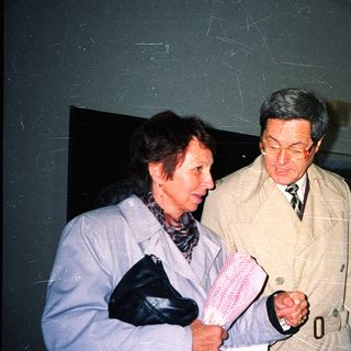 Two people in formal attire examining a handkerchief indoors.