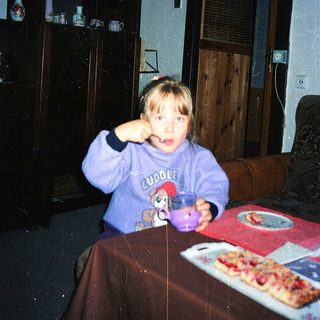 Child eating pizza indoors with cup.