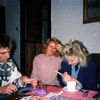 Three people sitting indoors, eating and drinking together.
