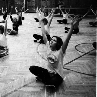 Group exercise class with seated participants raising arms.