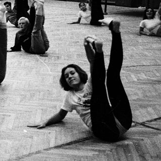 Group exercise class in gymnasium with stretching and movement.