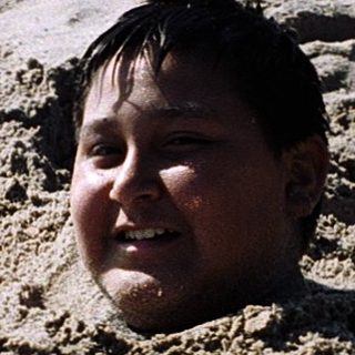Child buried in sand on beach.