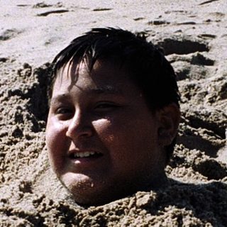 Child buried in sand on beach.