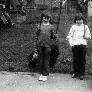 Two children standing outdoors with brooms.