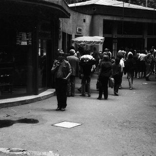 Crowded street scene with people queuing outside a store.