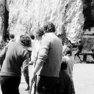 Group viewing large rock with statue.