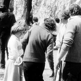 Group viewing large rock with statue.