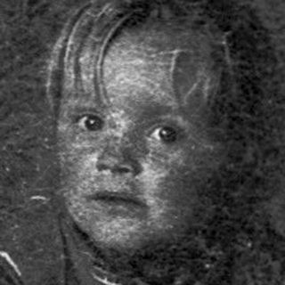 Child sitting at table with birthday cake and lit candles.