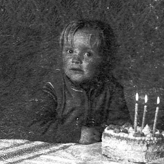 Child sitting at table with birthday cake and lit candles.