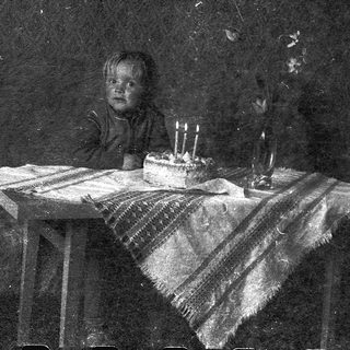 Child sitting at table with birthday cake and lit candles.