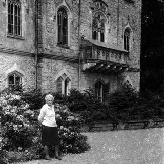 Person standing in front of historic stone building with arched windows.