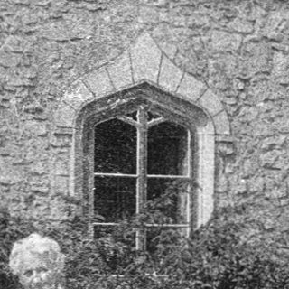 Old woman standing outdoors near historic stone building.