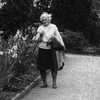 A woman walks along a garden path surrounded by flowers.