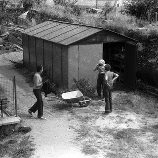 Two men working near a shed with wheelbarrow.