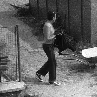 Two men working near a shed with wheelbarrow.