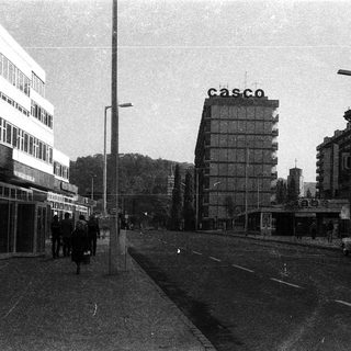 Urban street scene with mid-century buildings and "Casco" sign.