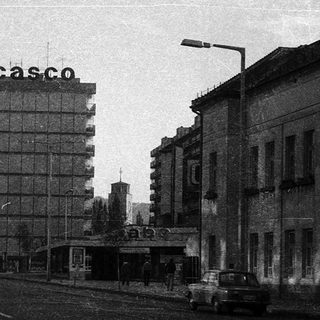 Urban street scene with mid-century buildings and "Casco" sign.