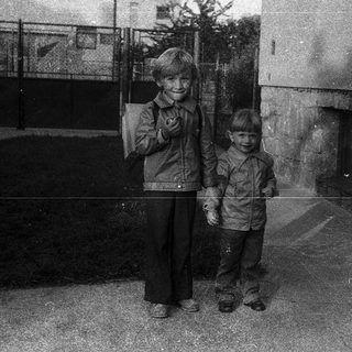 Two children posing outdoors in vintage military-style jackets.