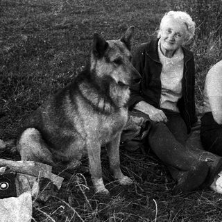 Two women and a German Shepherd in outdoor setting.
