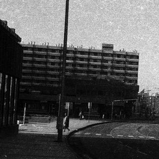 Urban street scene with mid-rise buildings and empty tracks.