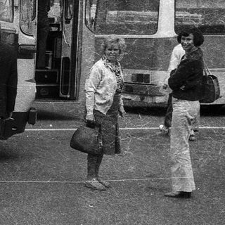People boarding a vintage bus at a bus stop.